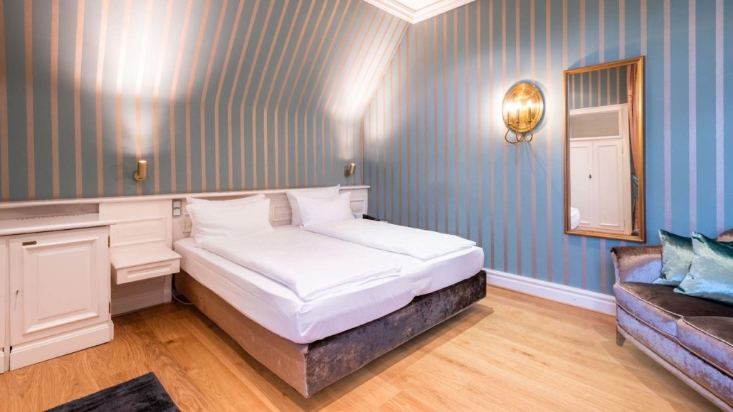 Doppelzimmer mit großem Bett Doppelzimmer mit zwei Einzelbetten, gestreiften Wänden, Holzfußboden, Sofa mit Kissen und großem Wandspiegel