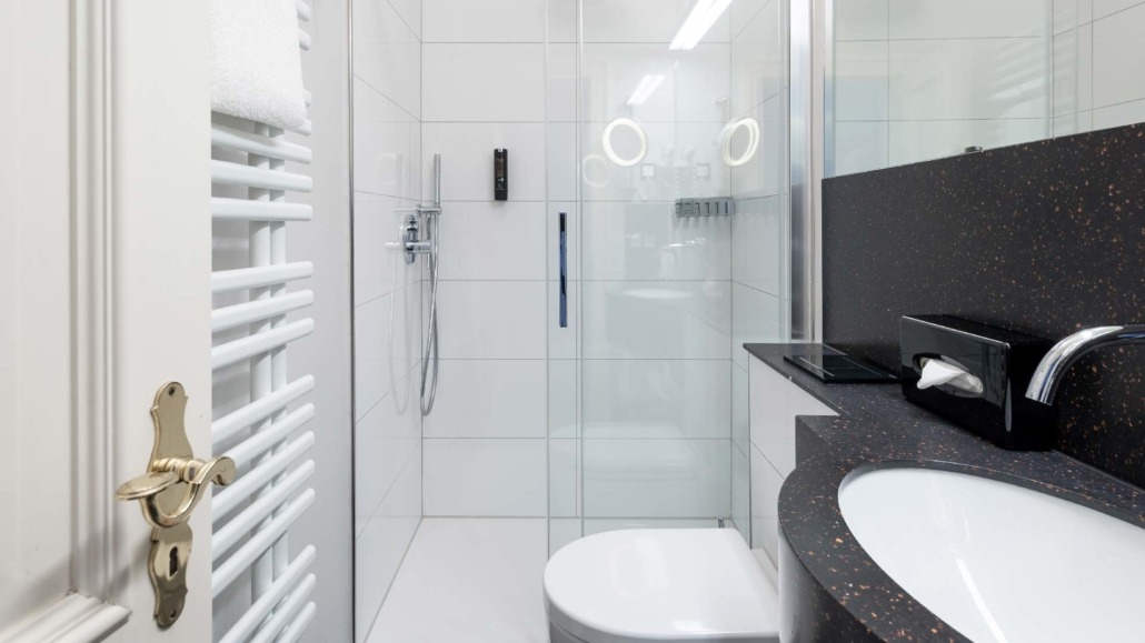 Badezimmer eines Einzelzimmers Kompaktes Badezimmer mit weißer Dusche, Toilette und schwarzer Waschtischplatte mit Waschbecken und Spiegel