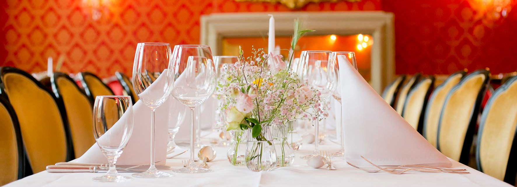 Festlich gedeckter Tisch mit weißen Servietten, Weingläsern und Blumenarrangement im Restaurant