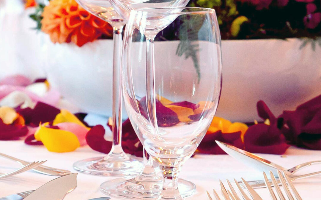 Gedeckter Tisch mit Weingläsern, Besteck und verstreuten Rosenblättern auf weißer Tischdecke