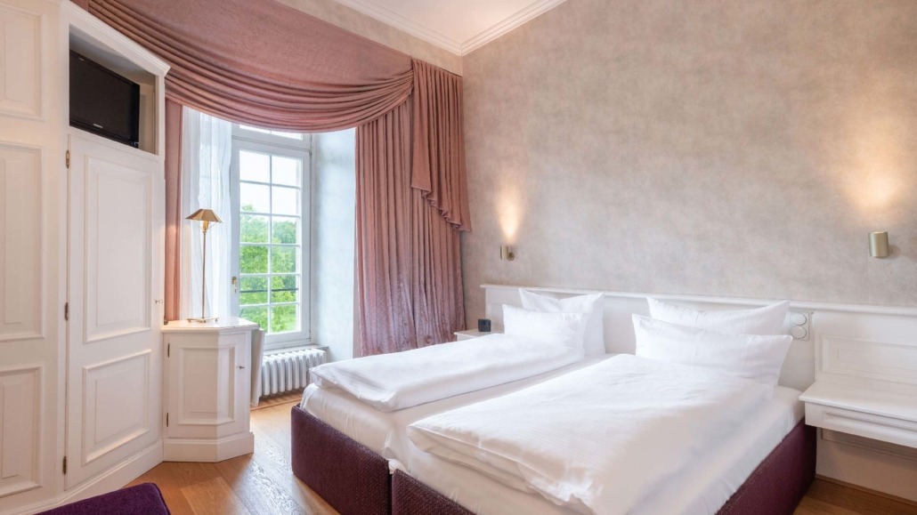 Suite mit Einzelbetten Suite mit zwei Einzelbetten, großen Fenstern mit rosa Vorhängen, weißem Schrank und Nachttischen