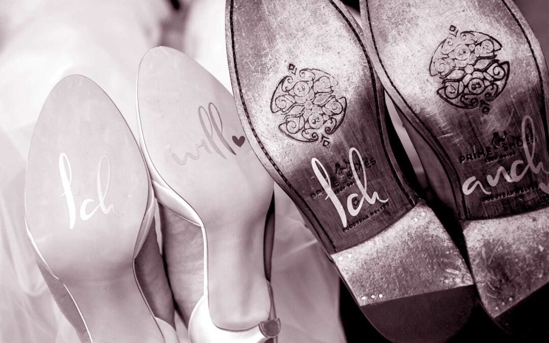 Zwei Paar Schuhe eines Hochzeitspaares mit den Worten 'Ich will', 'Ich auch' auf den Sohlen