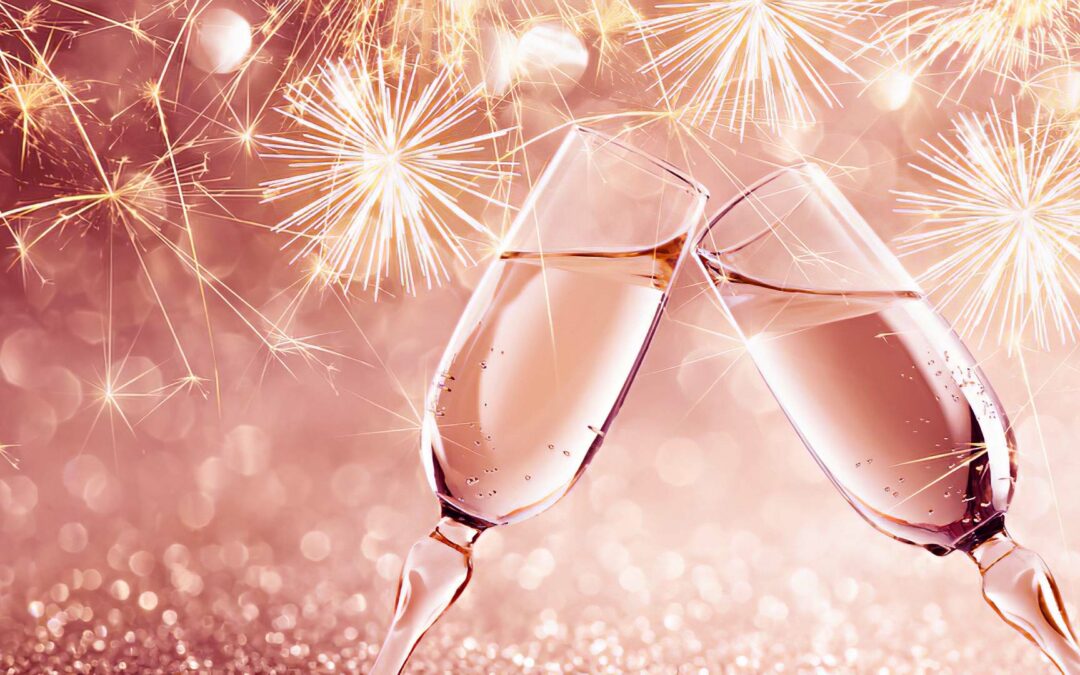 Zwei Sektgläser beim Anstoß zu Silvester mit Feuerwerk im Hintergrund