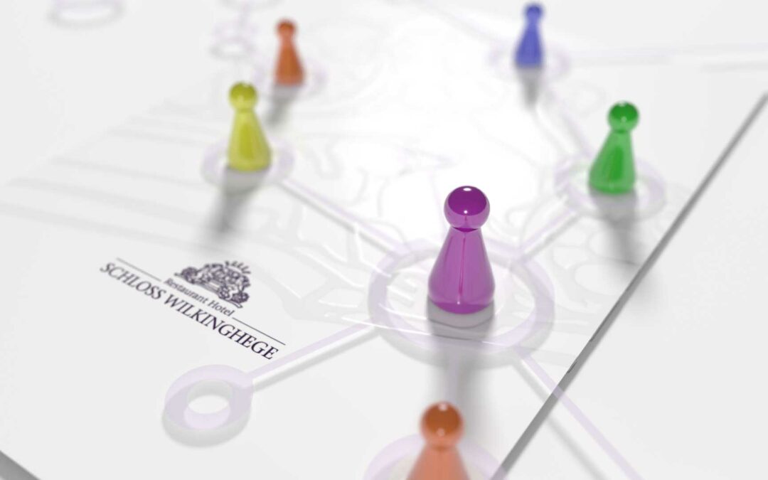 Spielfiguren in Gelb, Lila und Grün auf einem Plan mit dem Schriftzug 'Schloss Wilkinghege'